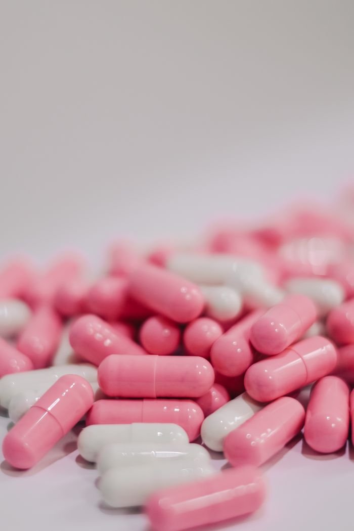 about-01 A close-up view of pink and white capsules on a white surface, indicating medication or vitamins.